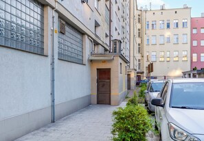 Um beco estreito na cidade, com fileira de carros estacionados de um lado e um edifício com fachada de vidro do outro.