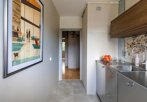 A modern kitchen with a stainless steel sink, a fruit bowl, and a large framed artwork on the wall.