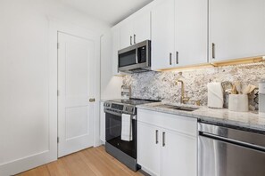 A modern kitchen with white cabinets, a stainless steel microwave, an oven, and a dishwasher. - The Palmetto Suite at One 01 (Savannah)