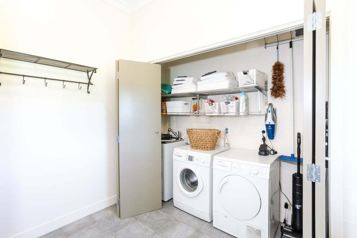 A laundry room with a washing machine, dryer, shelves with laundry baskets, and a vacuum cleaner.