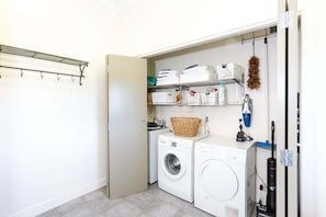 A laundry room with a washing machine, dryer, shelves with laundry baskets, and a vacuum cleaner. - Greystoke Lodge - Dalefield (Dalefield)