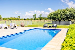 A rectangular swimming pool with a tiled edge, surrounded by a white fence, and a grassy area with trees and shrubs. - Greystoke Lodge - Dalefield (Dalefield)