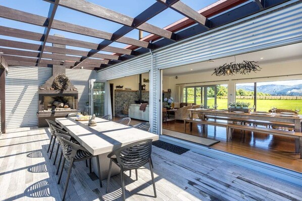 An outdoor dining area with a pergola, a stone fireplace, and a view of the countryside.