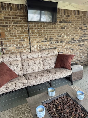Eine Ziegelwand, ein Flachbildfernseher, ein gemustertes Sofa und ein Tisch mit Kerzen und einer Schüssel mit Snacks.