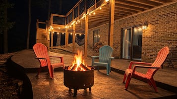 An outdoor patio with a fire pit, red and blue Adirondack chairs, and string lights.