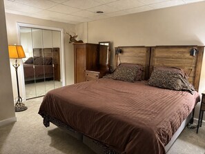 Ein Schlafzimmer mit einem großen Bett, einem Holz-Kopfteil, einem Spiegel, einem Kleiderschrank und einer Lampe.
