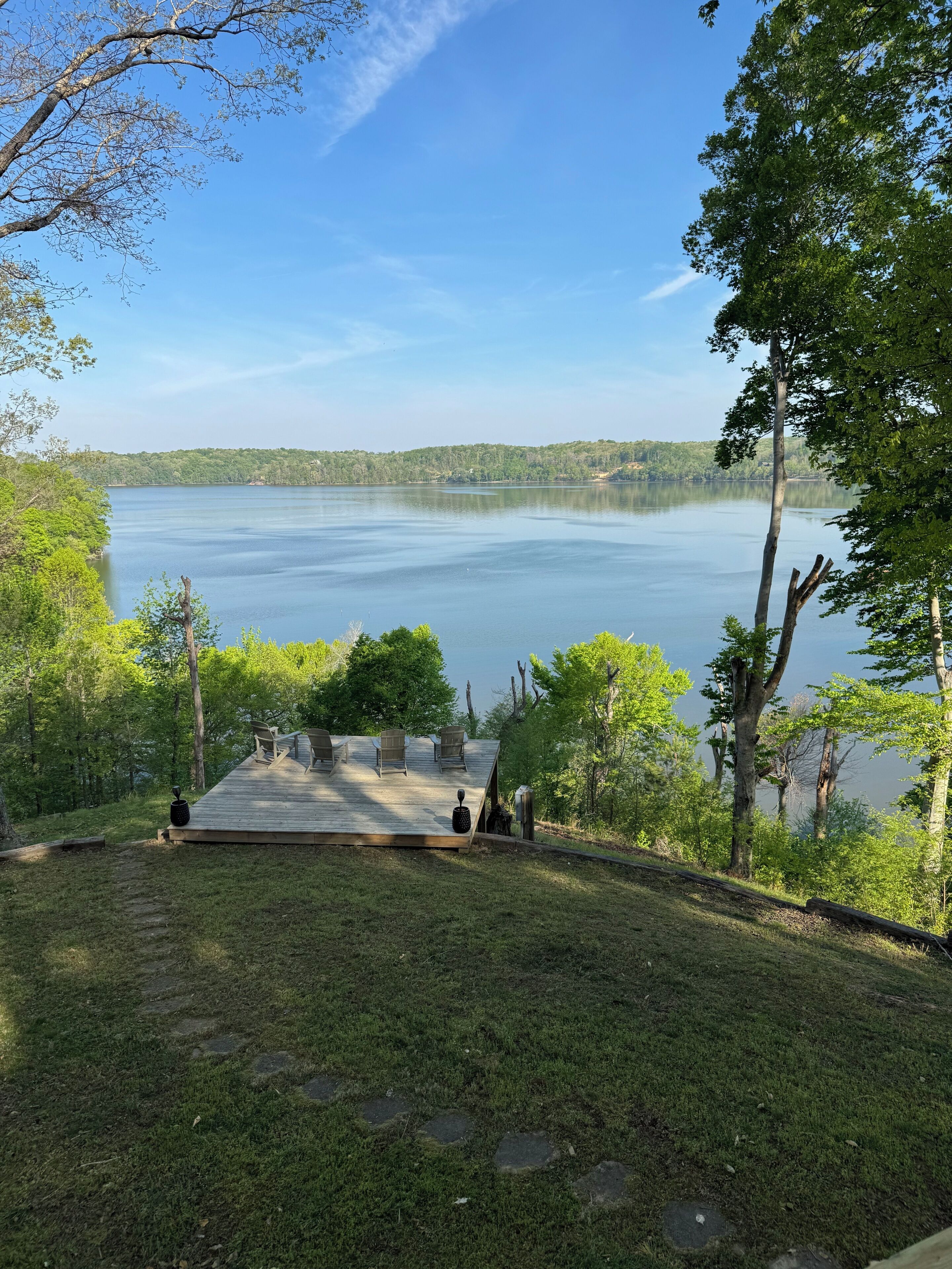 Eine Terrasse mit Stühlen mit Blick auf einen ruhigen See, umgeben von Bäumen.