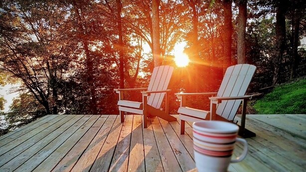 Une terrasse en bois avec deux fauteuils Adirondack et une tasse.