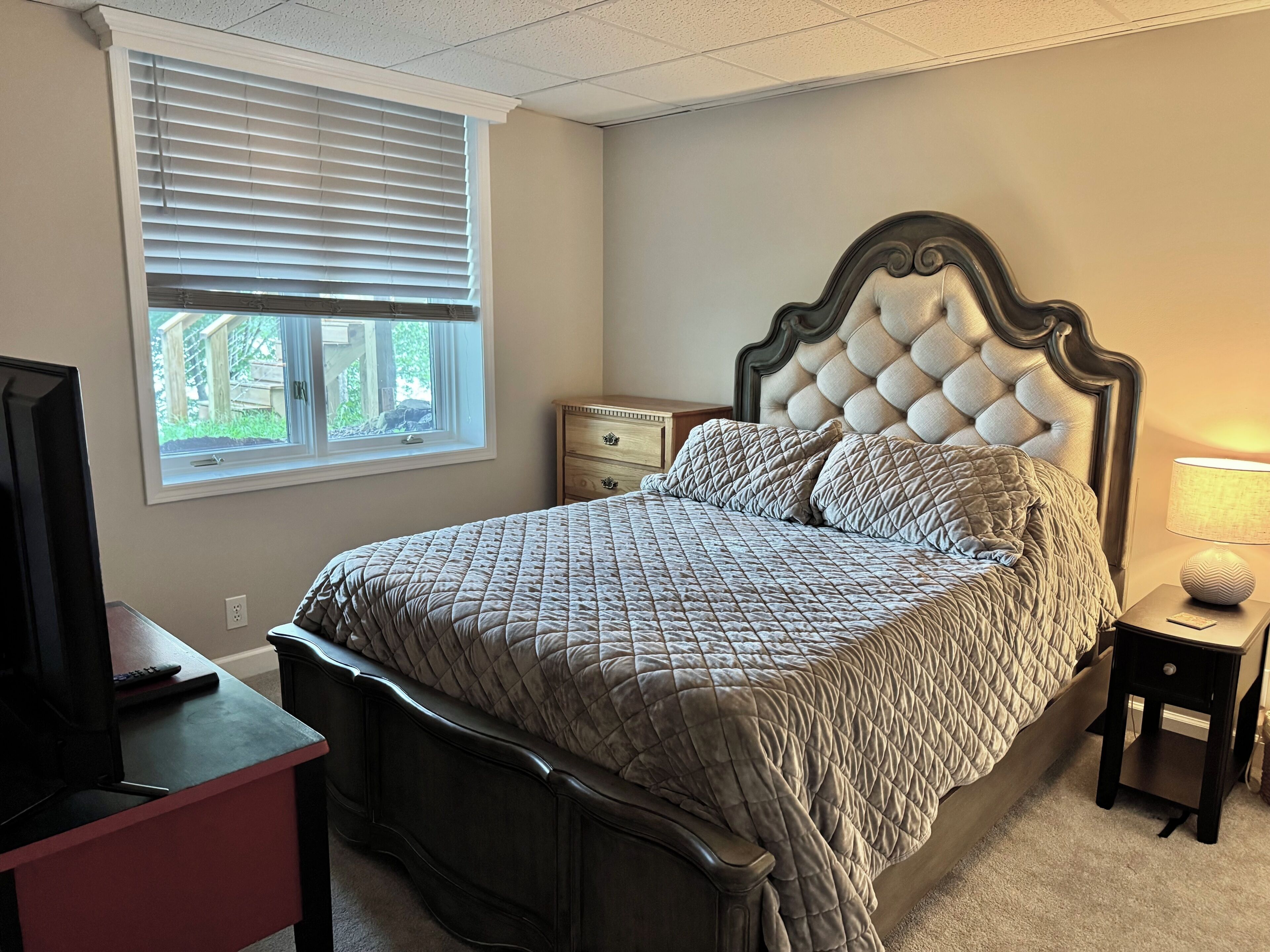 A bedroom with a bed, a nightstand, a dresser, a window, and a television.