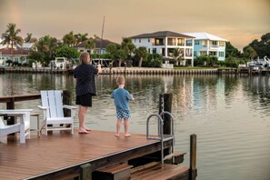 A wooden dock with a metal railing, a white chair, and a child standing on the dock. - Indian Rocks Beach New Waterfront Heated Pool & Spa  Golf Cart E-Bikes Kayaks Game Room Fire Pit Walking Distance to the Beach (Indian Rocks Beach)