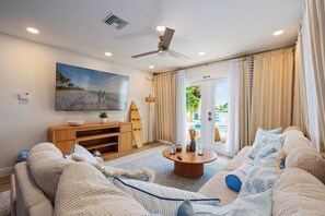 A living room with a flat-screen TV, a ceiling fan, a wooden entertainment unit, a round coffee table, and a sofa. - Indian Rocks Beach New Waterfront Heated Pool & Spa  Golf Cart E-Bikes Kayaks Game Room Fire Pit Walking Distance to the Beach (Indian Rocks Beach)