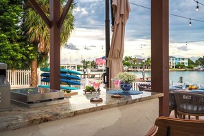 An outdoor bar area with a view of the marina, a grill, and seating. - Indian Rocks Beach New Waterfront Heated Pool & Spa  Golf Cart E-Bikes Kayaks Game Room Fire Pit Walking Distance to the Beach (Indian Rocks Beach)