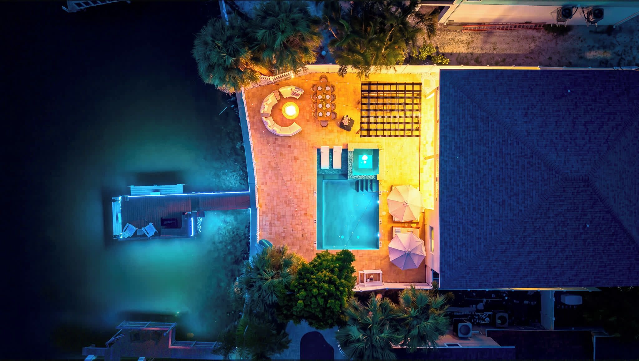 An aerial view of a property with a swimming pool, outdoor seating area, and a covered patio.