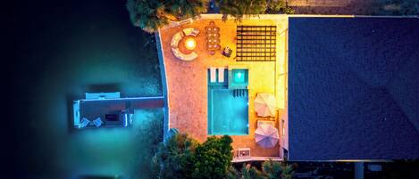 An aerial view of a property with a swimming pool, outdoor seating area, and a covered patio.