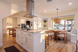 Une cuisine moderne dotée d’un îlot central, d’un coin repas avec des meubles en bois et d’une vue sur une étendue d’eau grâce à de grandes fenêtres.