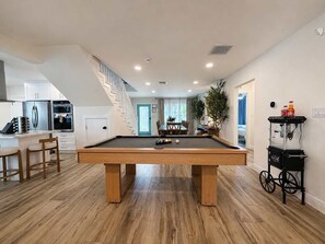 A modern living space with a pool table, kitchen, and dining area.
