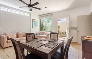 A living room with a sofa, a dining table with chairs, a ceiling fan, and a window with a view of greenery. - El Coral: apartment with rooftop lounge access minutes from 5 Avenida (Playa del Carmen)