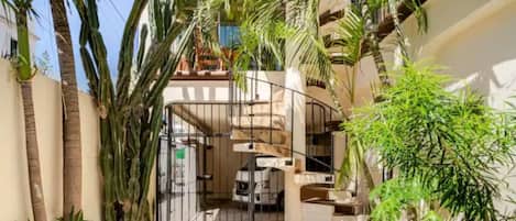 A residential building with a central staircase, surrounded by potted plants and palm trees.