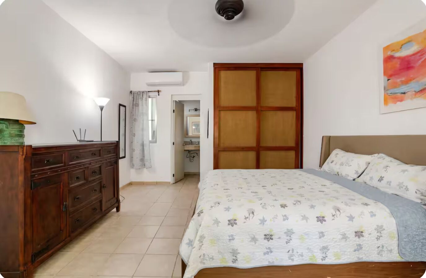 Quarto com cama, penteadeira e banheiro visível por uma porta aberta.
