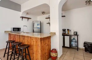 A kitchen with a central island, bar stools, a microwave, a refrigerator, and a water dispenser. - El Coral: apartment with rooftop lounge access minutes from 5 Avenida (Playa del Carmen)
