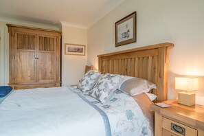 A bedroom with a wooden wardrobe, a bed with floral bedding, a nightstand with a lamp, and a framed picture on the wall. - Holiday Cottage in the Conwy Valley | Llwyn-Y-Coed-Isaf (Tal Y Bont)