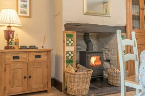 A cozy room with a wooden cabinet, a lamp, a fireplace with logs, and wicker baskets. - Views over Yr Wyddfa (Snowdon)  and the Welsh Highland Railway | Bron-Eifion (Rhyd Ddu)