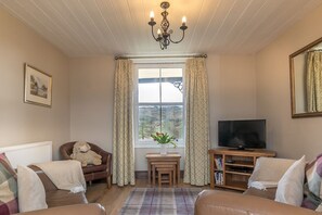 A cozy living room with a fireplace, a television, and a window with curtains. - Views over Yr Wyddfa (Snowdon)  and the Welsh Highland Railway | Bron-Eifion (Rhyd Ddu)