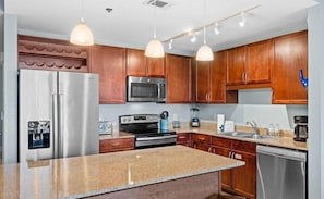 A kitchen with wooden cabinets, stainless steel appliances, granite countertops, pendant lighting, and a dishwasher. - Direct Garage Access, Lake View & 5 Pools | Laketown Wharf 226 (Panama City Beach)