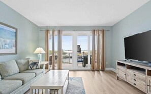 Ein Wohnzimmer mit einer Couch, einem Couchtisch, einem Fernseher und Blick durch eine Glastür.