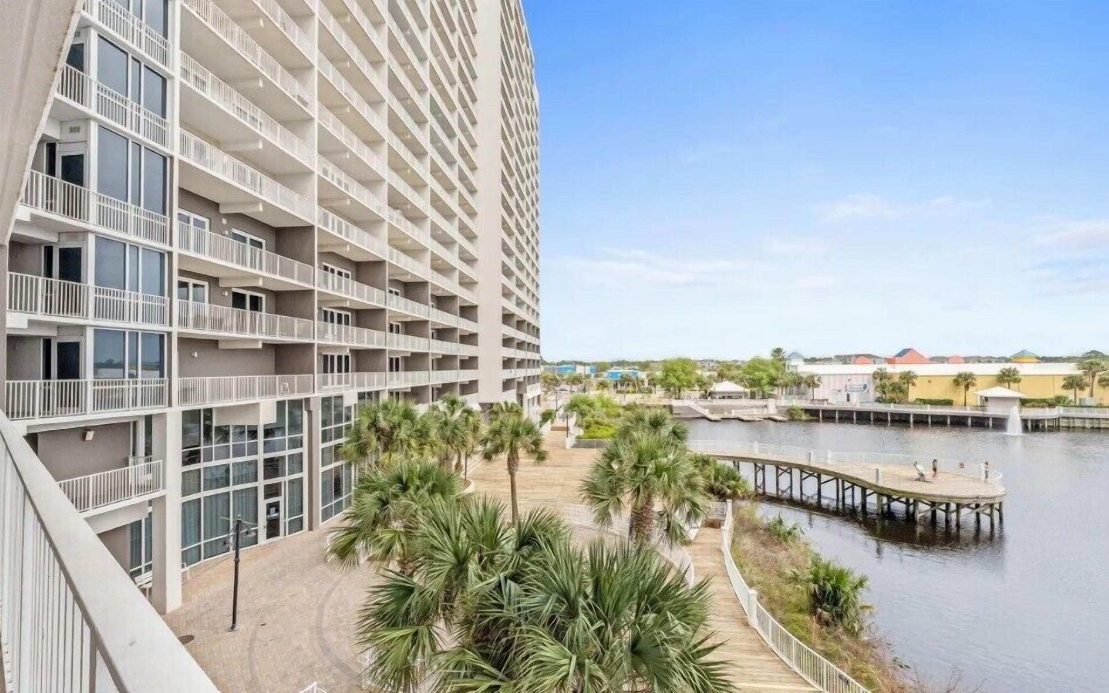 A high-rise hotel with multiple balconies, a waterfront promenade, and a dock extending into the water.