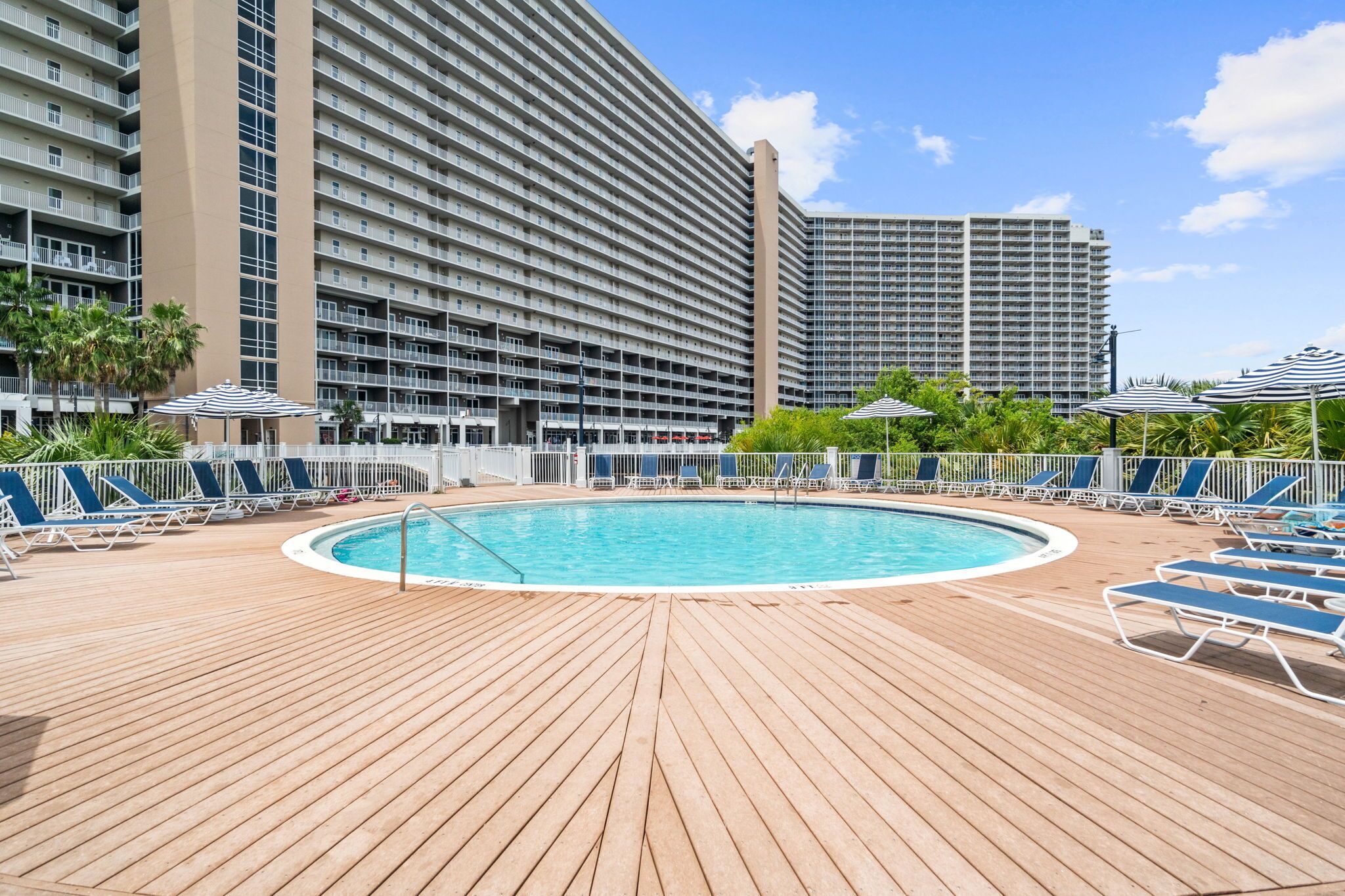 Zona de piscina con muelle de madera, sillas de descanso y sombrillas.