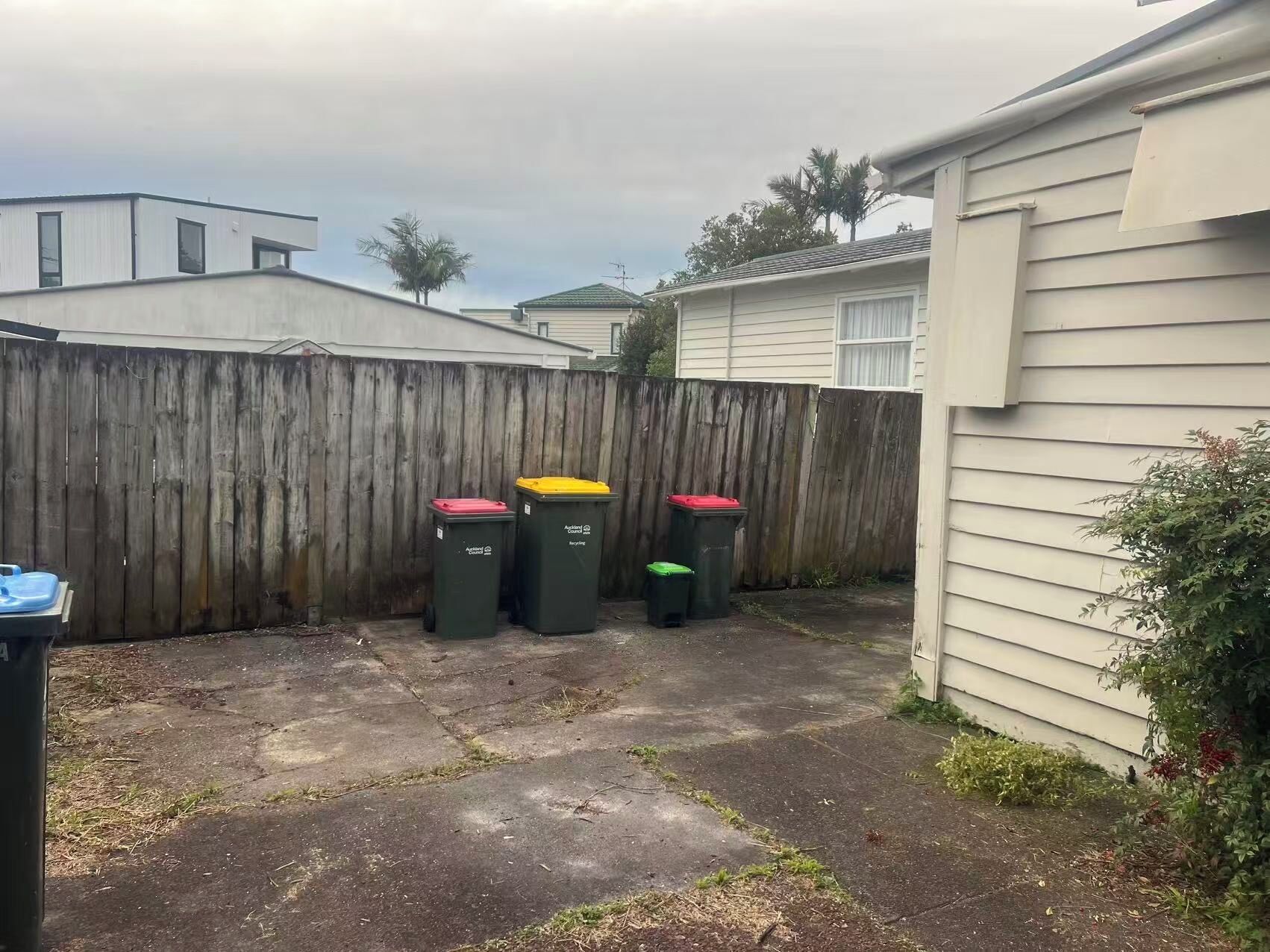 A backyard with a wooden fence, three trash bins, and a house.