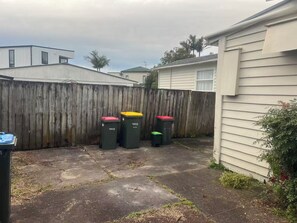 A backyard with a wooden fence, three trash bins, and a house. - 11 Double 4 Sofa Beds 5-bedroom House (Auckland)