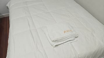A single bed with a white duvet and a folded towel with 'AWA' embroidered on it.