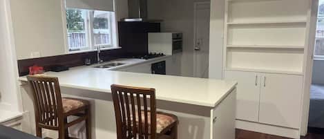 A kitchen with a central island, two wooden chairs, a black sofa, and a white cabinet.
