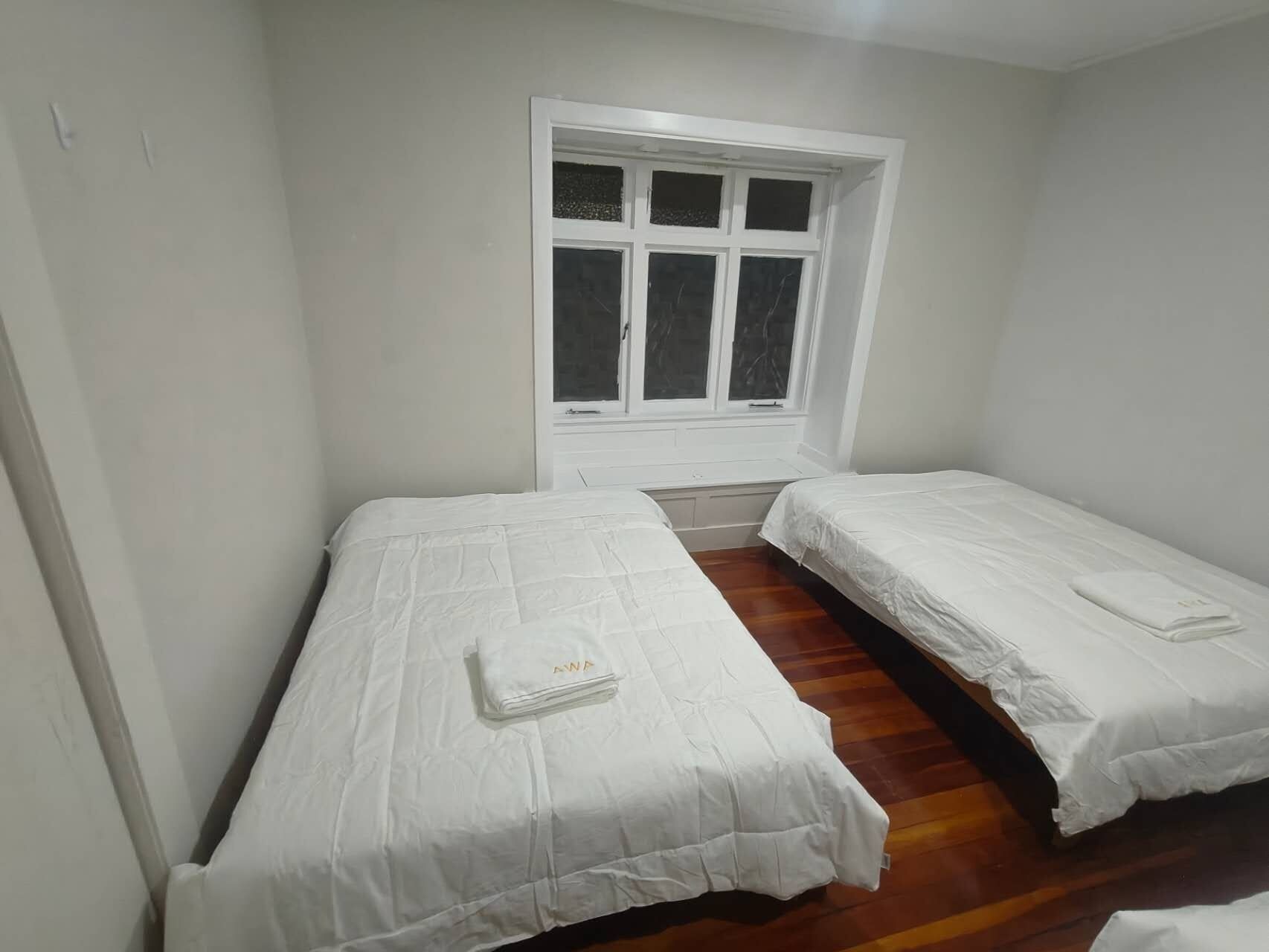 A room with two single beds, a window, and a wooden floor.