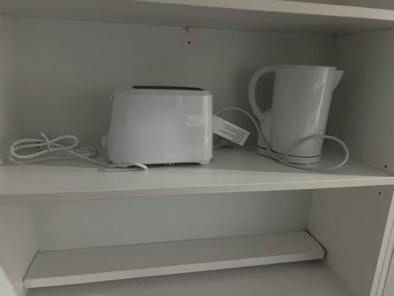 Una estantería blanca con un dispositivo electrónico blanco y una taza blanca.