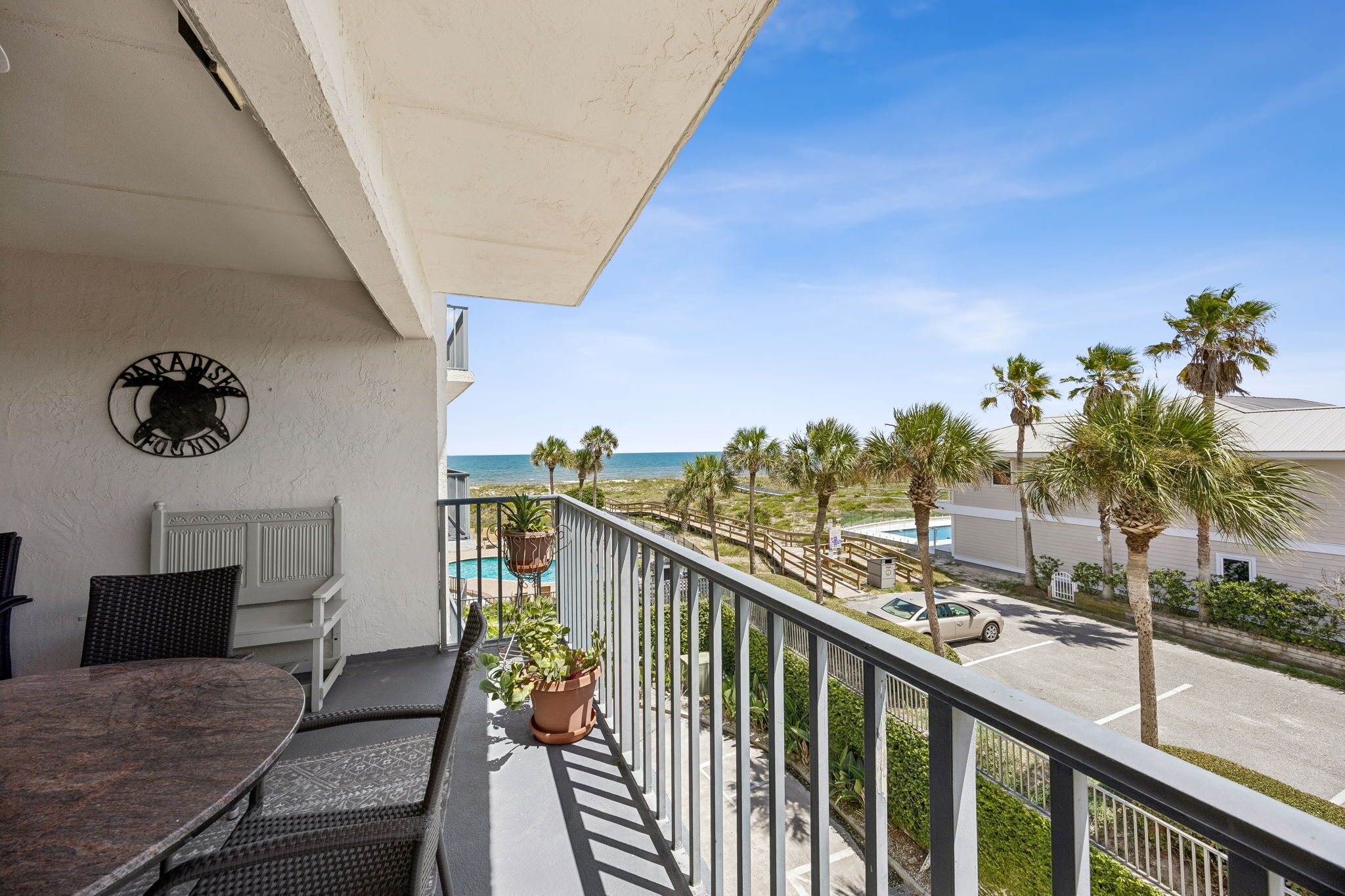 A balcony with a view of the beach, a pool, and palm trees.