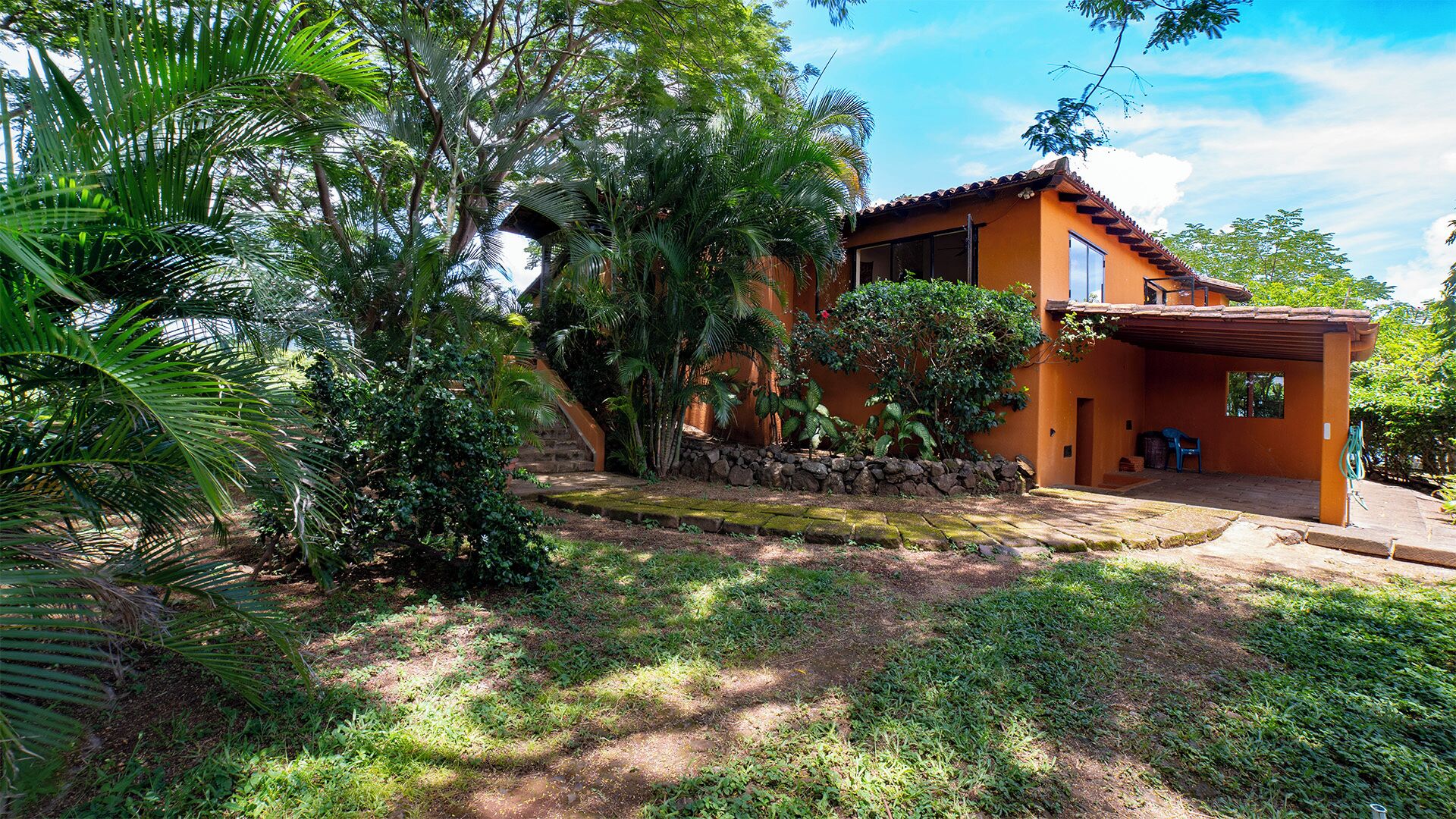 A house with a stone wall, a covered porch, and a garden with various plants.