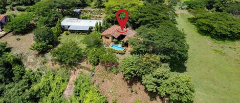 An aerial view of a property with a swimming pool, a house, and surrounding greenery.