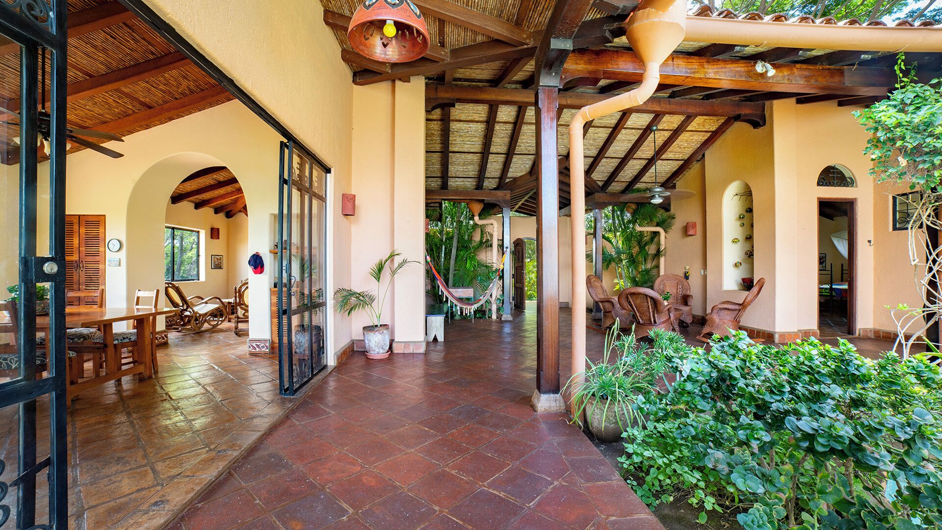 A covered outdoor area with a dining table and chairs, a hammock, and potted plants.