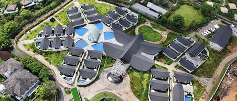 An aerial view of a resort with multiple bungalow-style accommodations, a central swimming pool area, and surrounding greenery.
