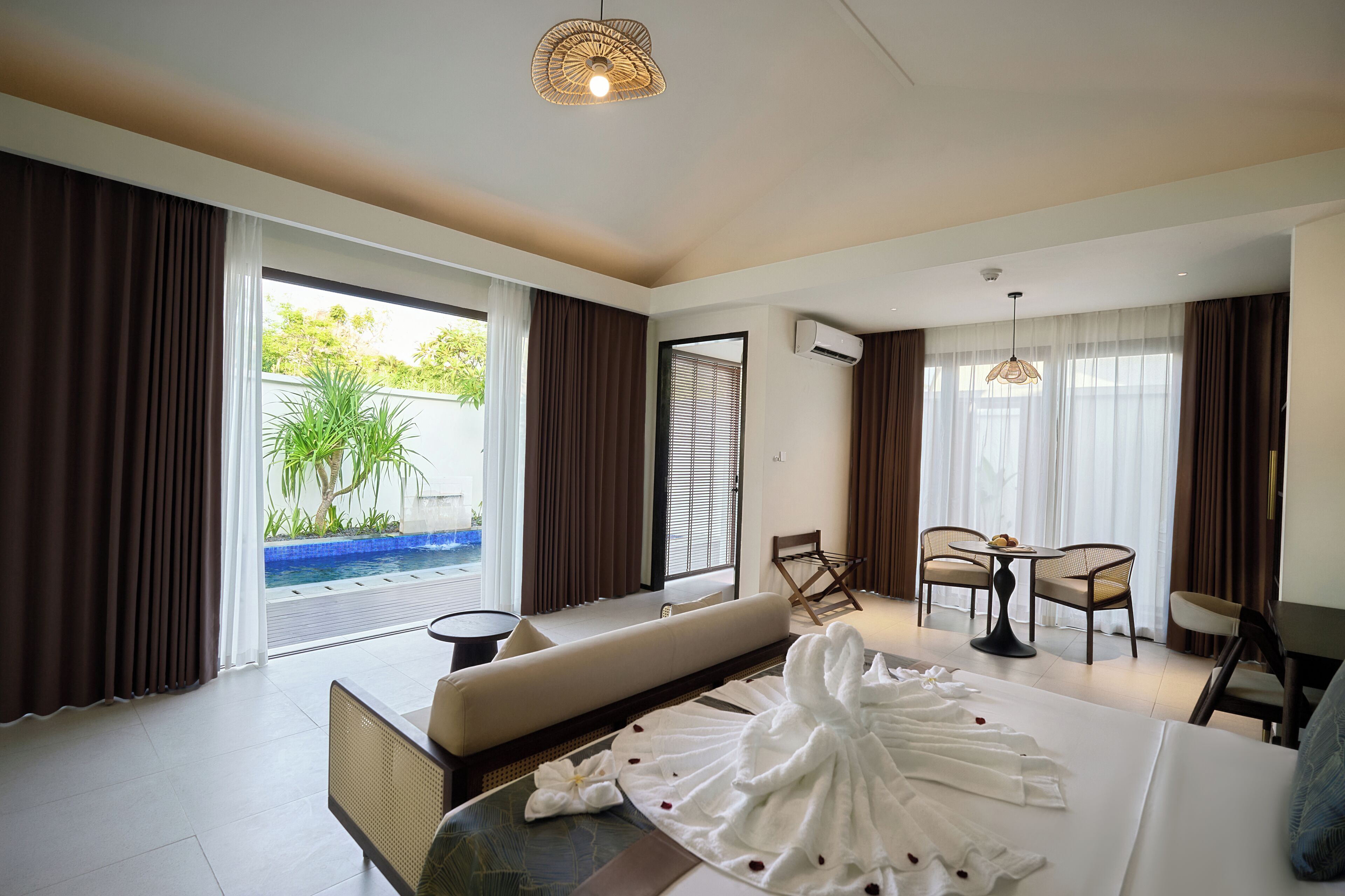 Ein Hotelzimmer mit Bett, einer Sitzecke, einem Esstisch mit Stühlen, einem kleinen Balkon mit Pool und Blick ins Grüne.