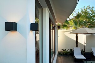 A modern outdoor seating area with a white wall, a large umbrella, and a lounge chair.