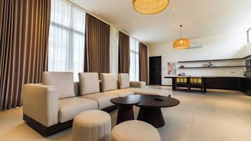 Een moderne woonkamer met een hoekbank, poefjes, een salontafel en een eethoek met stoelen.