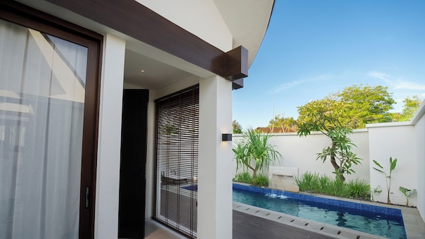 A modern outdoor pool area with a clear blue sky, a wooden deck, and a white wall with a window.