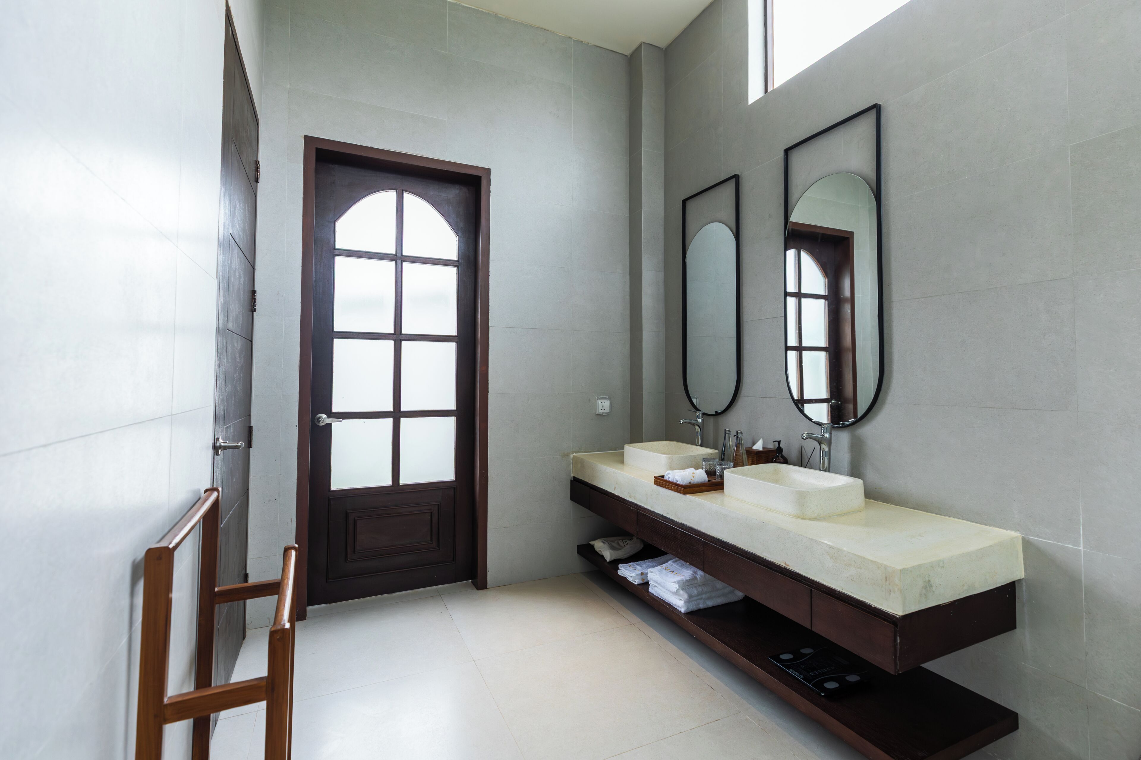 A modern bathroom with a large arched door, a double sink vanity, and two wall-mounted mirrors.