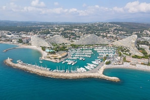 A marina with numerous boats docked, surrounded by a curved stone breakwater, and adjacent to a large hotel complex with multiple buildings. - 2 Bedrooms Apartment Sea View & Garage Marina, Villeneuve-Loubet, France (Villeneuve-Loubet)