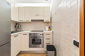 Een compacte keuken met witte kastjes, een roestvrijstalen oven en een betegelde achterwand.