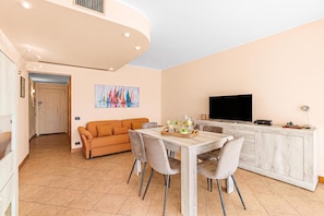 A modern living room with a sofa, dining table, and chairs, a kitchen area with a TV, and a painting on the wall. - 2 Bedrooms Apartment Sea View & Garage Marina, Villeneuve-Loubet, France (Villeneuve-Loubet)